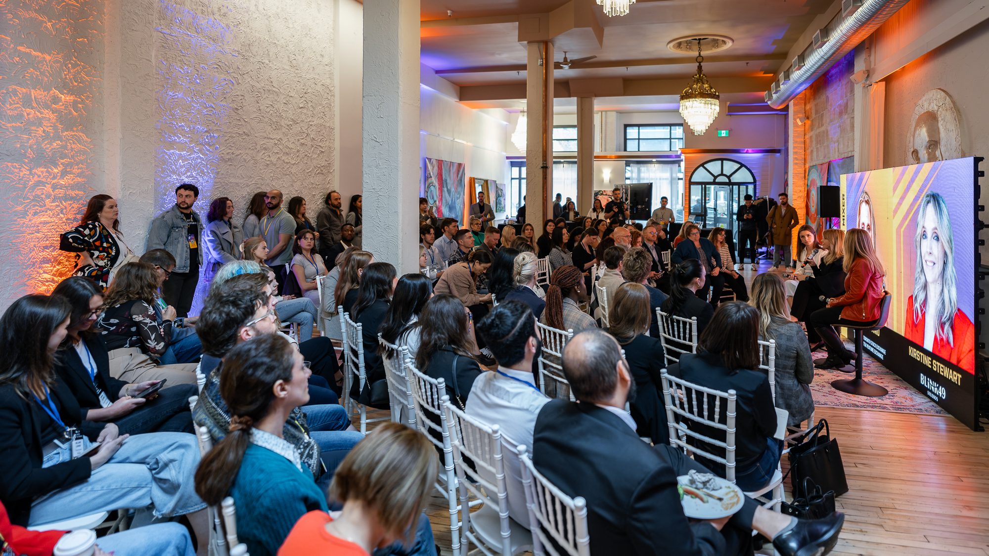 A panel talk in a white heritage venue at a Co.Labs event, Saskatoon, speaker portraits shown on a large LED screen.